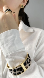 Detailed view of model wearing a gold leopard print bangle, matching ring and stud earrings