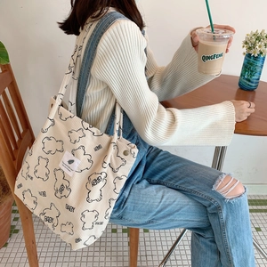 Detail view of cream corduroy tote bag with black bear print worn by a model