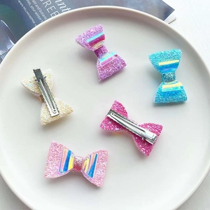Five assorted glitter bow hair clips for girls displayed on a white round plate