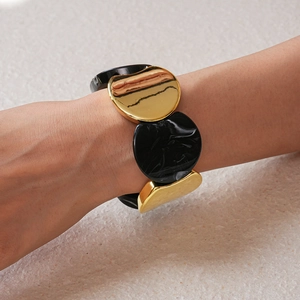 Dettaglio del bracciale geometrico in metallo dorato e resina marmorizzata sul polso