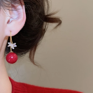 Detail of elegant gold-plated earrings with red resin bead and crystal flower on model