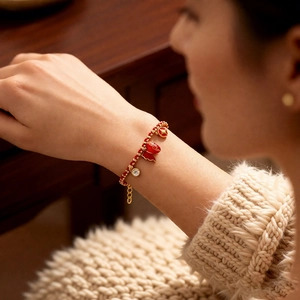 Close-up of red beaded bracelet with 18k gold butterfly and zircon charms on wrist