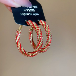 Macro detail of large gold hoop earrings encrusted with sparkling red crystals on S925 studs