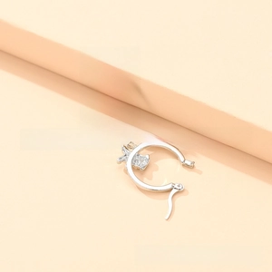 Detail shot of silver hoop earrings featuring cute cartoon cow charms on orange stands
