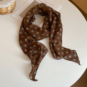Detailed view of dark brown polka dot silk scarf draped over a minimalist white table