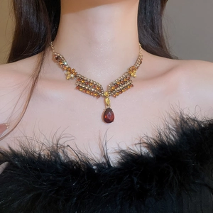 Macro shot of V-shaped gold necklace with red teardrop crystal and orange rhinestones