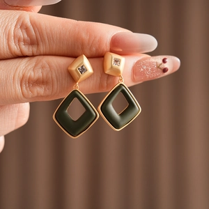 Detailed macro view of geometric earrings with gold finish and dark green rhombic pendants