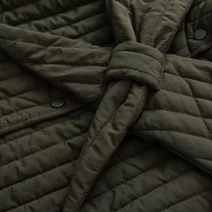 Detail of dark olive quilted jacket showing button closure and matching waist tie texture