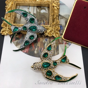 Détail artistique de broches hirondelle en or et argent avec des pierres vert émeraude
