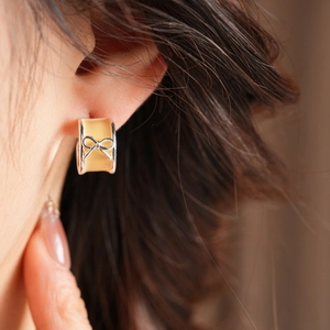 Close-up of yellow enamel C-shaped earrings with silver metal bow on earlobe