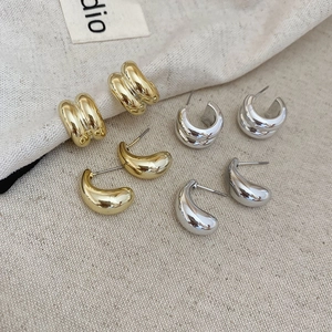 Macro view of four pairs of polished gold and silver water drop and C-shaped earrings