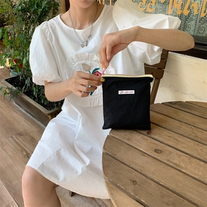 Portable black nylon pouch with contrast zipper held by a model in an outdoor cafe setting