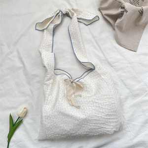 Close-up of white polka dot canvas bag with blue trim and adjustable ribbon strap