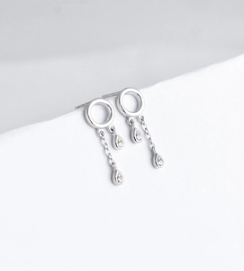 Detail of silver drop earrings with tassel and zircons against a white geometric background