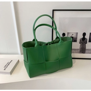 Close-up of green woven leather tote bag on white surface with decorative books