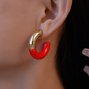 Close-up of C-shaped earrings with red acrylic splicing and gold metal finish