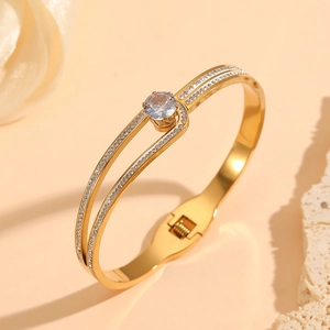 Gros plan d'un jonc ouvert doré avec zircon central et pavé de pierres sur fond beige