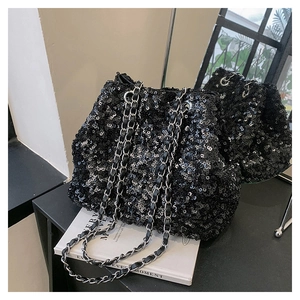 Close-up of black sequined bucket bag with metal chain strap on white books