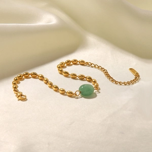 Detail of gold beaded bracelet with green oval gemstone on a cream satin background