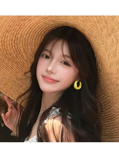 Detail of yellow C-shaped geometric acrylic earrings worn by model with summer straw hat