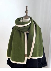 Detail of green knitted scarf with cream white contrast border on a mannequin