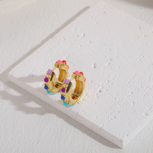 Detail of bohemian gold-plated hoop earrings with colorful beads on a marble stand