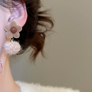 Close-up of woman wearing flocking flower and pompom drop earrings in autumn style