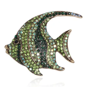 Elegant tropical fish brooch with green crystals and vintage gold finish on white background