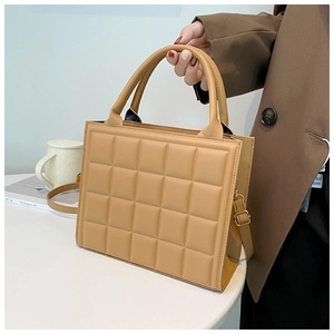 Detail of camel quilted crossbody bag with matte finish and adjustable strap on a white desk