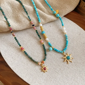 Détail de colliers faits main avec perles d'eau douce, perles vertes et pendentifs soleil