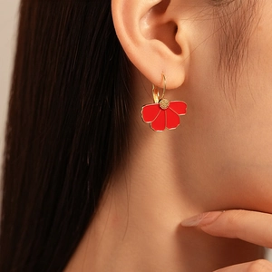 Detail of red enamel flower earring with gold-plated petals on model ear