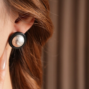 Close-up of minimalist round pleated stud earrings with silver texture and black border