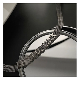 Bracelet en maille d'acier avec pendentifs GOOD LUCK sur une surface réfléchissante