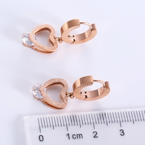 Rose gold heart earrings with frosted texture and zircon inlay against a scale