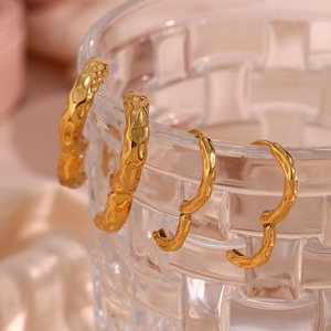 Detailed close-up of golden irregular hammered surface hoop earrings on glass rim