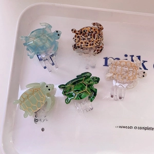 Five turtle-shaped cellulose acetate hair claws in various marble colors on a tray