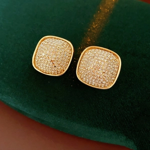 Macro shot of square gold stud earrings featuring micro-paved cubic zirconia on green velvet