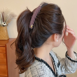 Détail d'une pince banane en tissu marron fixant une queue de cheval sur un mannequin