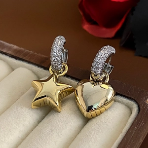 Macro shot of asymmetric gold star and heart earrings with micro-paved zircons on silver hooks