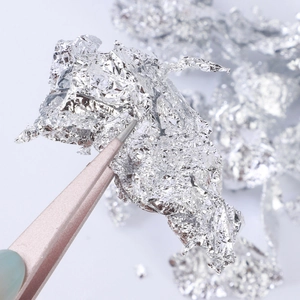 Macro view of silver metallic foil flakes picked up with tweezers for DIY nail art decoration