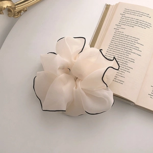 Detail of a large cream mesh scrunchie with black contrast trim on an open book
