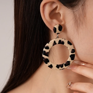 Close-up of model wearing large leopard print hoop earrings made of faux leather texture
