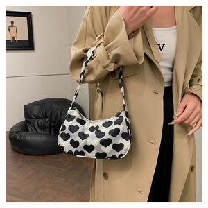 Gros plan du sac sous le bras en toile à motif cœur noir et blanc porté avec un trench kaki