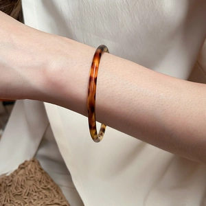 Detail of elegant amber tortoiseshell resin bangle worn by a model in soft lighting