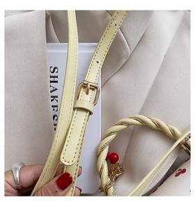 Detail of light yellow leather bag showing woven metal handle and adjustable strap buckle