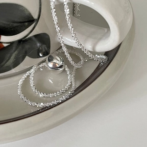 Polished S925 sterling silver ball pendant necklace draped on a white ceramic cup
