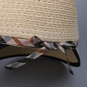 Close-up of woven straw sun hat with elegant plaid ribbon bow and natural fiber texture
