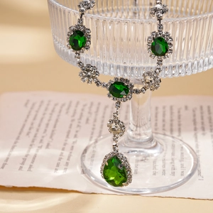 Detail of vintage emerald pendant necklace with crystals draped over glassware
