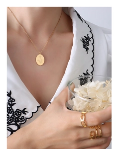 Macro view of 18K gold necklace with engraved floral pendant on white embroidered top