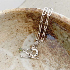 Macro shot of silver link bracelet with green gemstone drop and classic T-bar toggle clasp